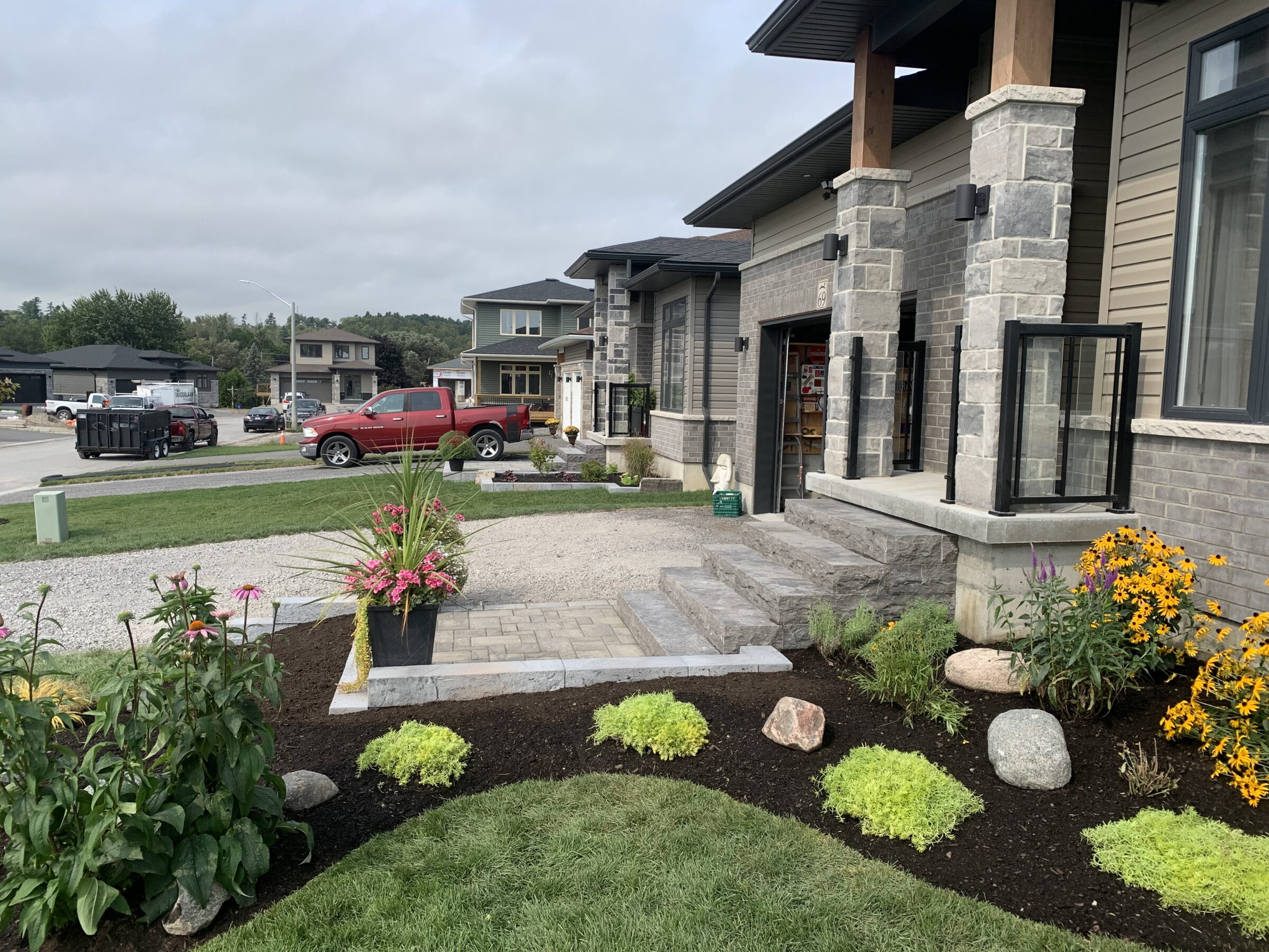 Suburban neighborhood with modern stone house, landscaped front yard, red truck, and overcast sky; no landmarks or historical buildings present.