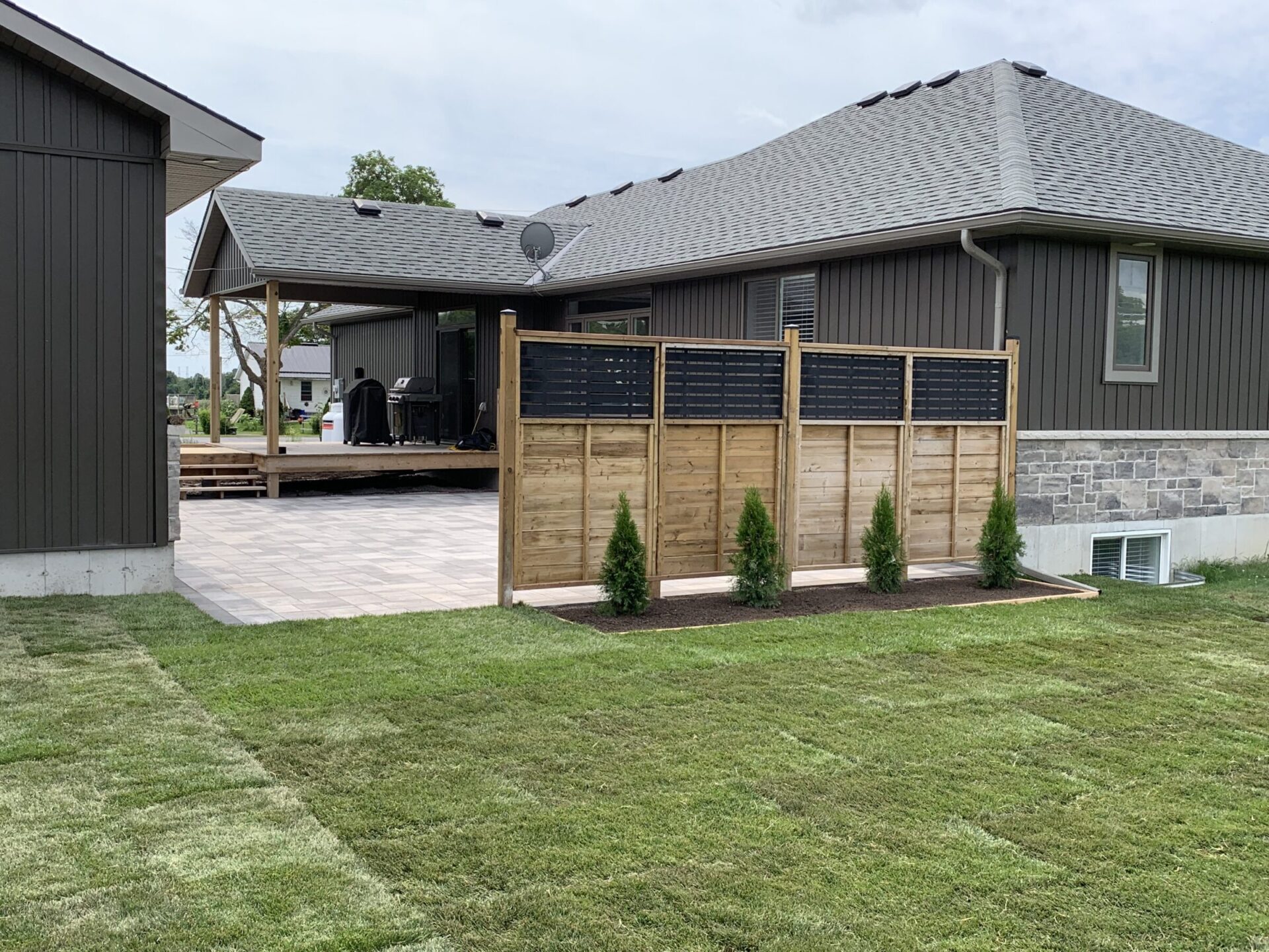 A house with a patio, privacy fence, and a small tree garden in a neatly landscaped yard, featuring outdoor furniture and grill.