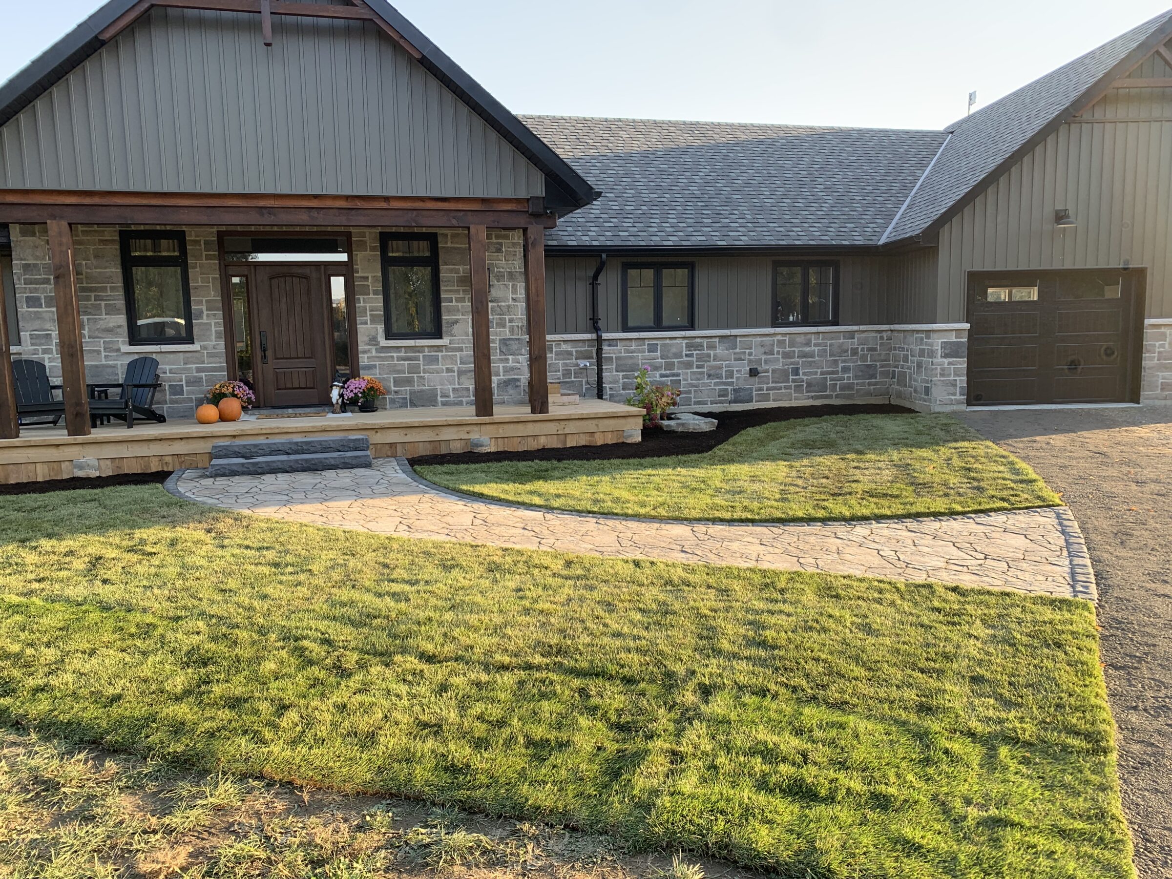 A modern house with a stone facade, wooden porch, and fresh landscaping. Pumpkins and flowers decorate the entrance for a cozy feel.