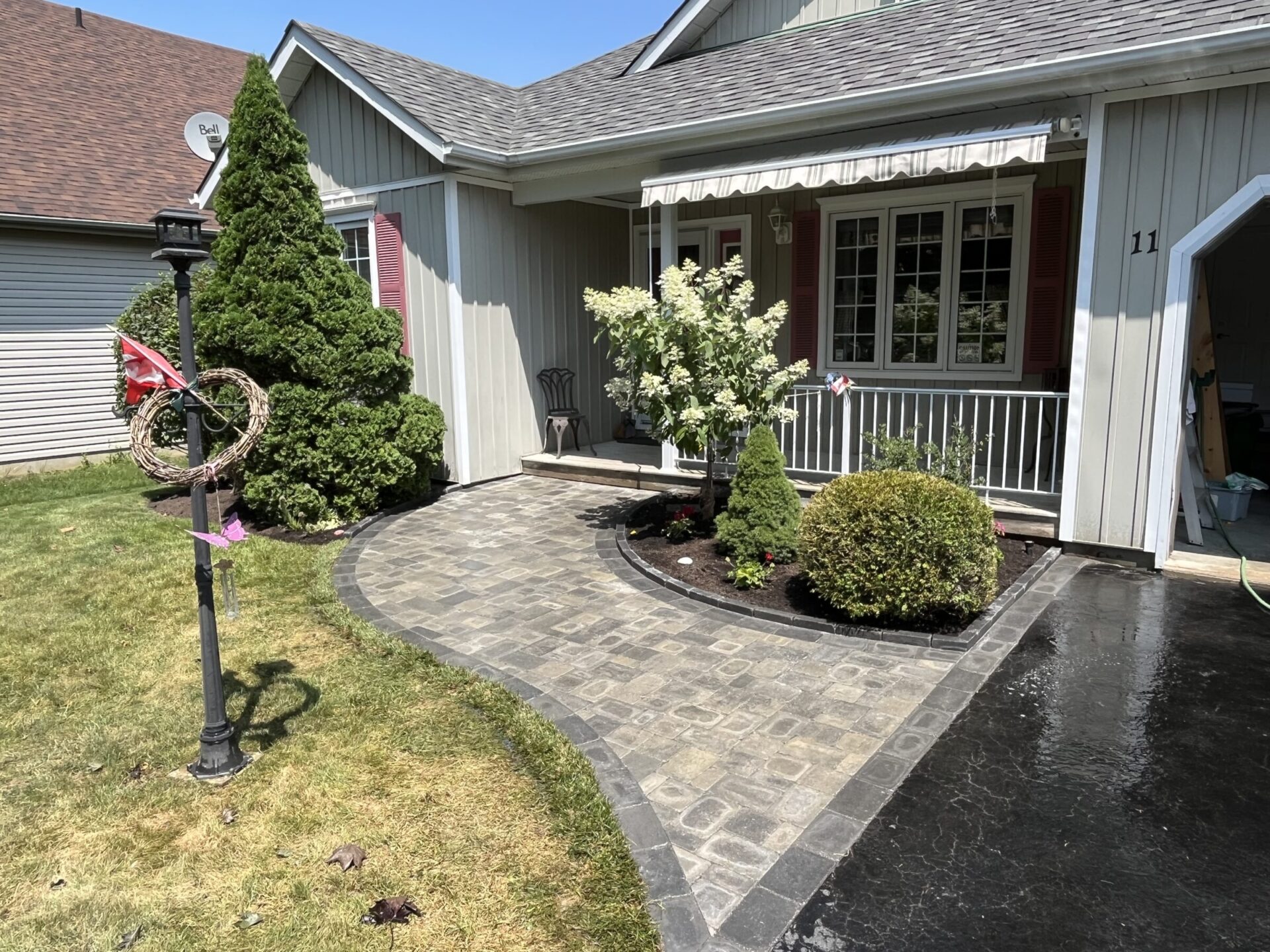 A quaint house with a manicured garden, stone pathway, and Canadian flag decoration, showcasing an inviting suburban setting on a sunny day.