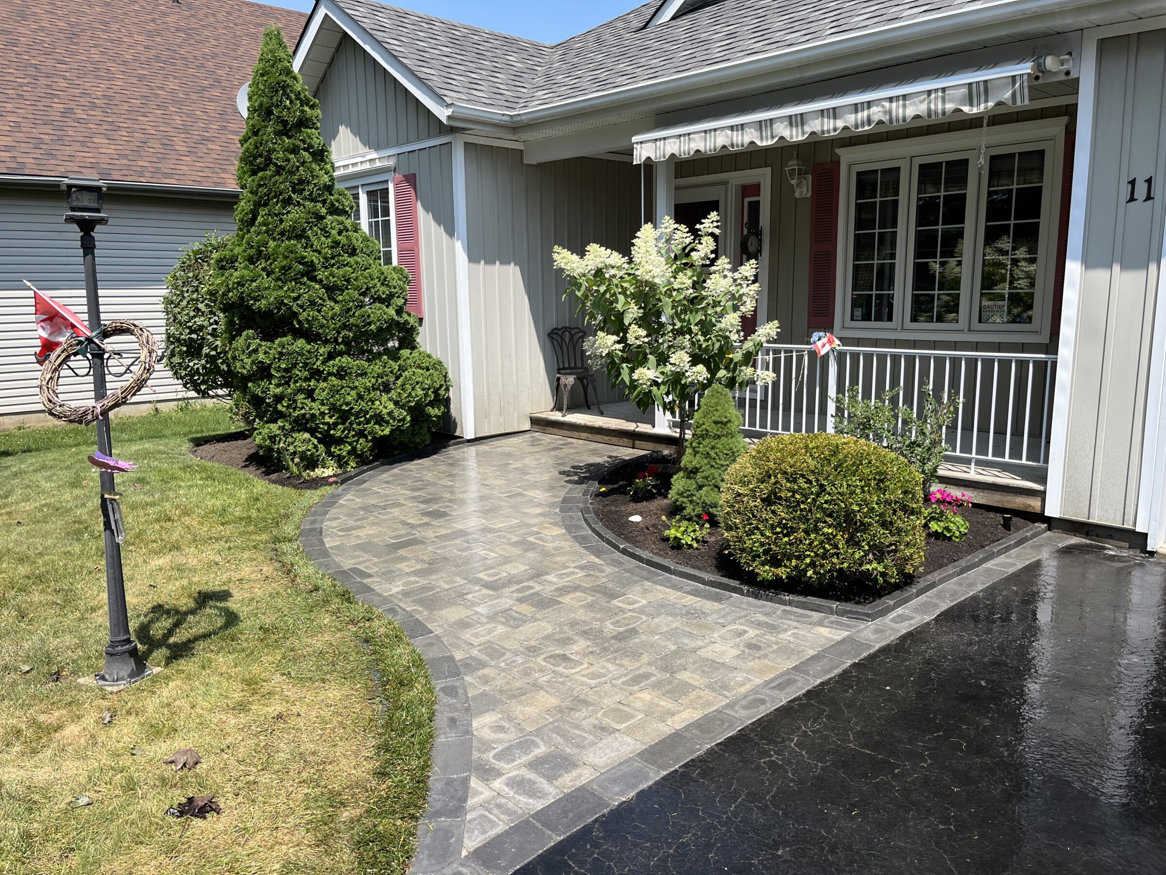 A residential house features a manicured garden, pathway, porch, and decorative wreath on a lamppost. No recognizable landmarks or historical buildings present.