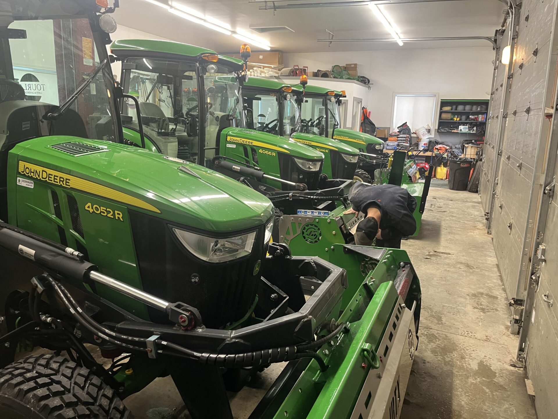 A person works on green John Deere tractors in a well-lit garage with equipment and tools.